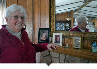 Older woman stands at mantle smiling and looking at pictures